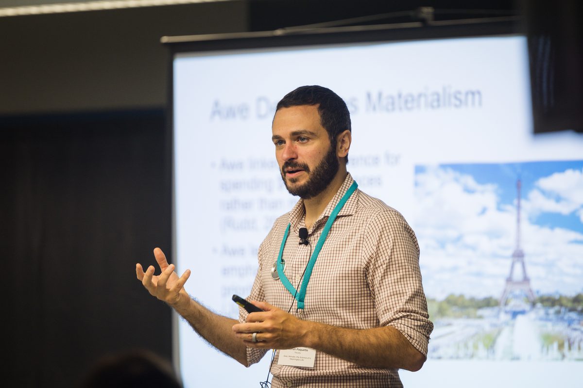 A clinician presents to an audience, gesturing as he speaks beside a projected slide.